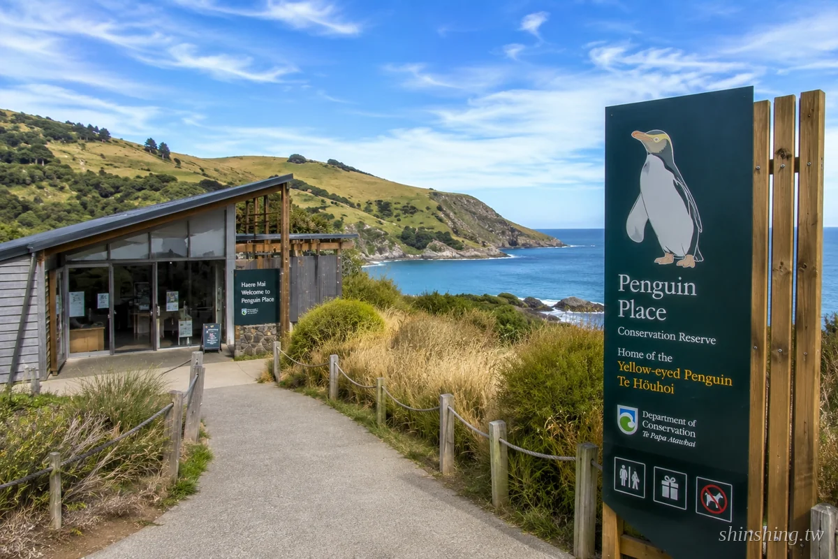 但尼丁 Penguin Place 保育區入口與招牌,寫著 Home of the Yellow-eyed Penguin,背後是奧塔哥半島海岸