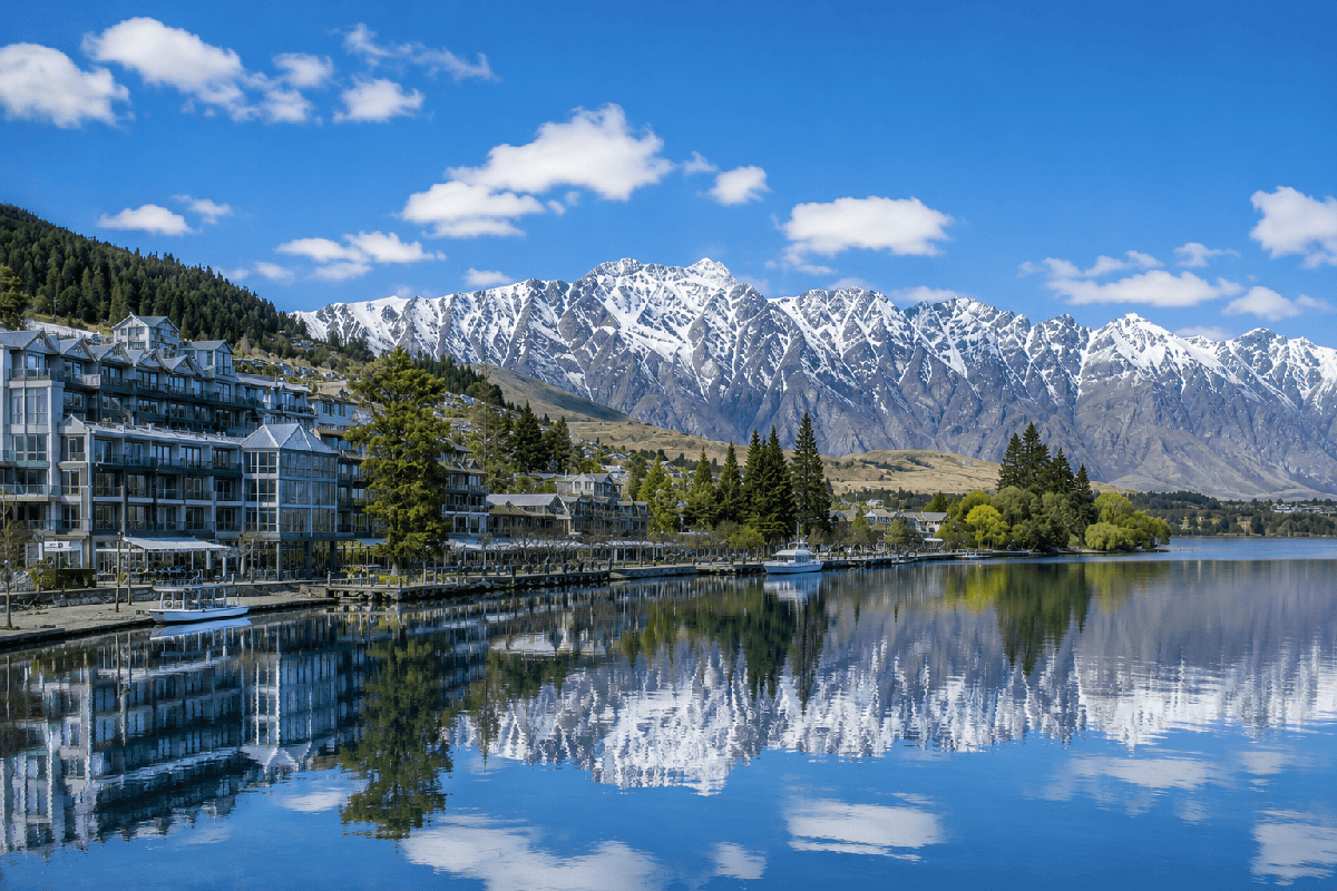 皇后鎮瓦卡蒂普湖畔住宿全景，湖面倒映雪山，遠處是 The Remarkables 山脈