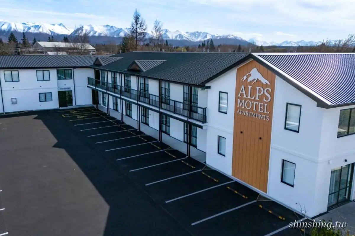 Alps Motel & Apartments 的白色兩層建築,山形招牌寫著 ALPS MOTEL APARTMENTS,前方是整排停車格,遠方是南阿爾卑斯雪山