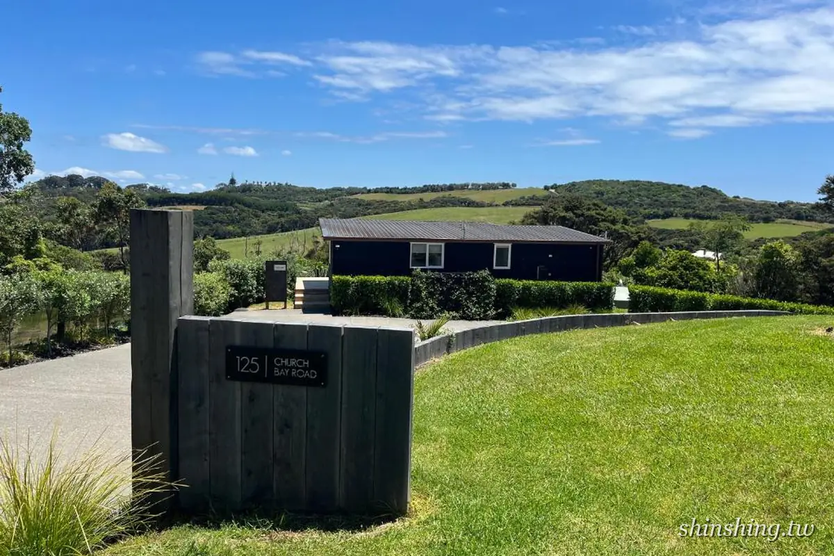 125 Church Bay Cabins 入口門牌與黑色木屋,背後為懷赫克島葡萄園山丘