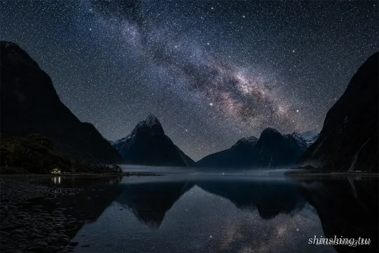 米佛峽灣夜空的銀河橫跨山峰之間，Mitre Peak 的剪影完整倒映在無風的水面上