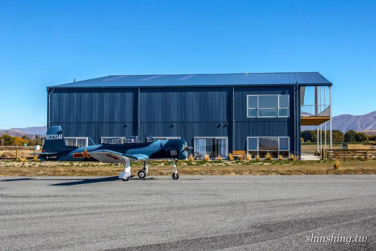 Pukaki Air Lodge 的深灰色機棚式建築與二樓陽台,前方停放一架藍色老式螺旋槳飛機