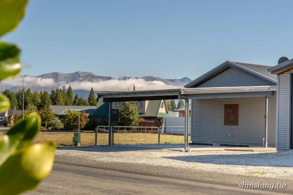 Twizel Cottages 的灰色鐵皮小屋,外牆標著大大的數字 2,前方有車棚,遠方是雲海與山脈